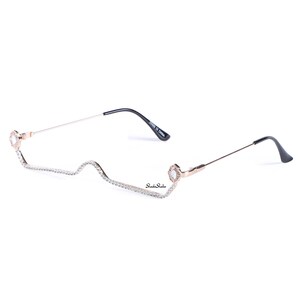 May include: Rose gold metal frame glasses with clear lenses and rhinestones along the frame. The glasses have a unique, curved shape.
