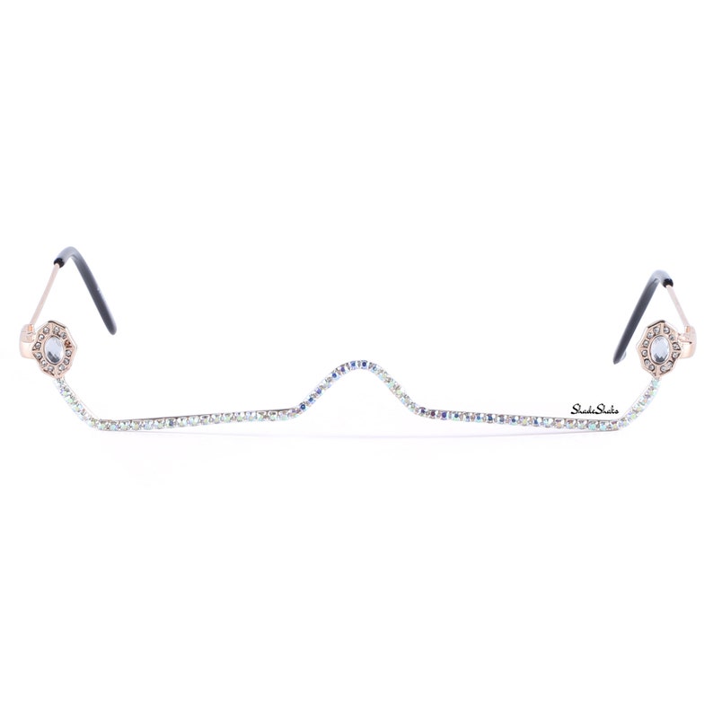 May include: Gold-tone glasses with a clear rhinestone chain connecting the temples. The chain has a slight wave pattern. The brand name "Shade Shade" is printed on the chain.