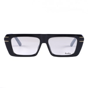 May include: Black rectangular eyeglasses with gold accents and clear lenses. The brand name "Studio Stile" is printed on the right lens.