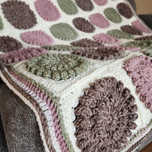 May include: A crocheted blanket with a white background and large, colorful circles in shades of brown, pink, and green.