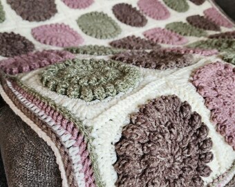 May include: A crocheted blanket with a white background and large, colorful circles in shades of brown, pink, and green.