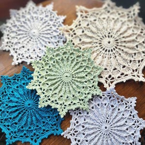 Puede incluir: Cinco manteles individuales de ganchillo en varios colores, incluyendo blanco, verde y azul. Los manteles individuales son todos circulares y tienen un diseño delicado y de encaje.