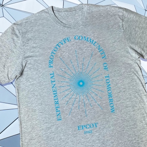May include: Gray t-shirt with a blue graphic of a sunburst and the text "EXPERIMENTAL PROTOTYPE COMMUNITY OF TOMORROW EPCOT 1982"