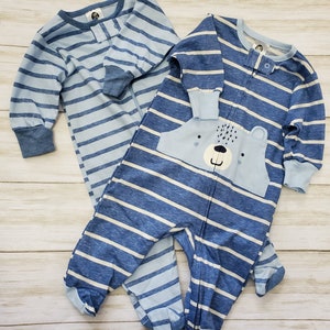 May include: Two blue and white striped baby footed pajamas. One pajama has a bear face on the chest. Both pajamas have long sleeves and a button or zipper closure. The pajamas are made of a soft material.