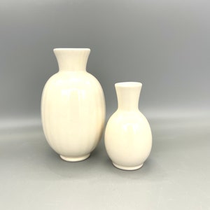 Op de afbeelding: Twee witte keramische vazen, een groter dan de andere, met een ronde, bolle vorm. Beide vazen hebben een gladde, glanzende afwerking.