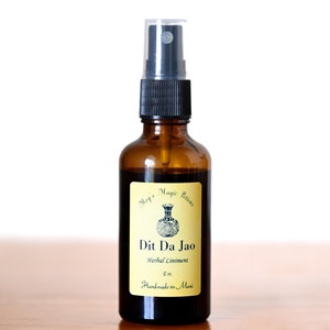 May include: A brown glass spray bottle with a black cap and a clear plastic cover. The bottle has a yellow label with the text "Meg's Magic Potions" and "Dit Da Jao Herbal Liniment 2 oz. Handmade on Maui."