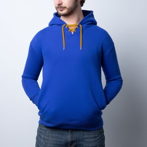 May include: A royal blue hoodie with a lace-up neckline and a kangaroo pocket. The hood has a drawstring, and the long sleeves have ribbed cuffs. The lace-up detail is a mustard yellow color.