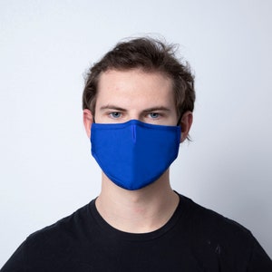 May include: A person wearing a solid blue face mask. The mask covers the nose and mouth. The person is looking directly at the camera.