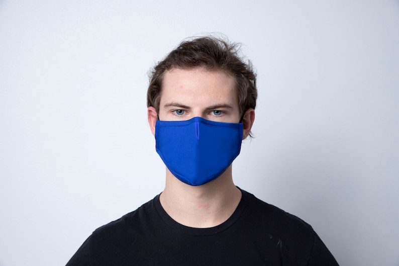 May include: A person wearing a solid blue face mask. The mask covers the nose and mouth. The person is looking directly at the camera.