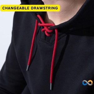May include: Close-up of a black hoodie with a red drawstring. The drawstring is threaded through the hood and is adjustable. The text "CHANGEABLE DRAWSTRING" is in a yellow box in the upper left corner. A small logo is on the lower right.