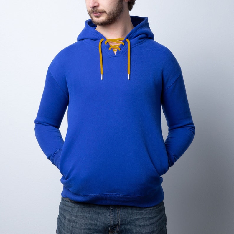 May include: A royal blue hoodie with a lace-up neckline and a kangaroo pocket. The hood has a drawstring, and the long sleeves have ribbed cuffs. The lace-up detail is a mustard yellow color.