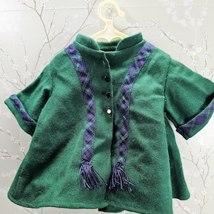 May include: A green jacket with a stand-up collar and short sleeves. The jacket features a plaid pattern in purple and blue along the front and on the sleeve cuffs. The jacket has black buttons and a single white button. The jacket has two decorative tassels.