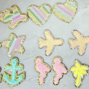 May include: A collection of colorful, beaded patches in various shapes, including airplanes, hearts, stars, anchors, flamingoes, and palm trees. Each patch has a gold glitter border. The patches are in pastel colors.