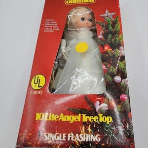 May include: A vintage Christmas tree topper in a box. The angel figurine has blonde hair and a white dress. The box is red with the text "10 Lite Angel Tree Top" and "Single Flashing". The box also has the text "A White Christmas".