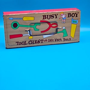 May include: A vintage metal toy tool chest with a red and tan exterior. The chest has a black handle and features a cartoon boy with the text "BUSY BOY TOOL CHEST with SAFE VINYL TOOLS".
