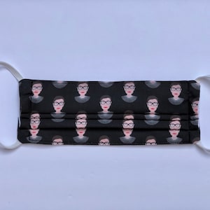 May include: Black face mask with a repeating pattern of a woman wearing glasses and a white collar. The mask has white elastic straps.