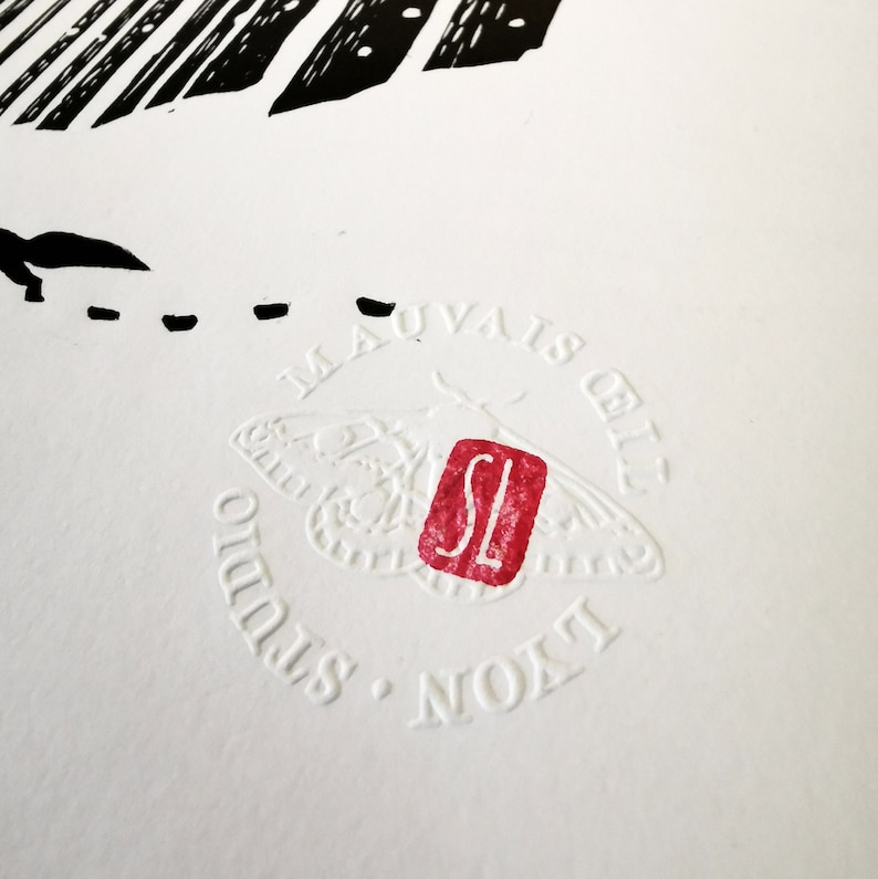 May include: Close-up of a white print with black and red accents. The print features a moth design, the text "MAUVAIS &OElig;IL STUDIO LYON", and a red stamp with the letters "SL".