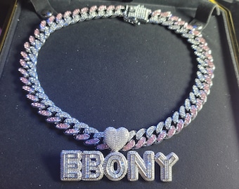 May include: A silver and pink diamond-encrusted Cuban link chain necklace with a heart pendant and a nameplate pendant that reads "EBONY".