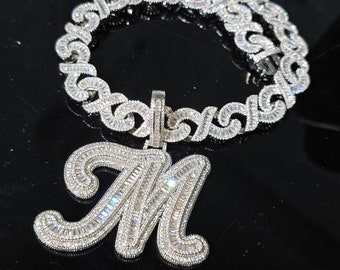 May include: A silver chain necklace with a large, diamond-encrusted letter M pendant. The chain is made of interlocking links, each set with small diamonds.