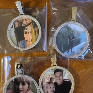 May include: Three gold-tone pendants with round photo inserts. Each pendant has a diamond-like design around the photo insert. The photos show different people.