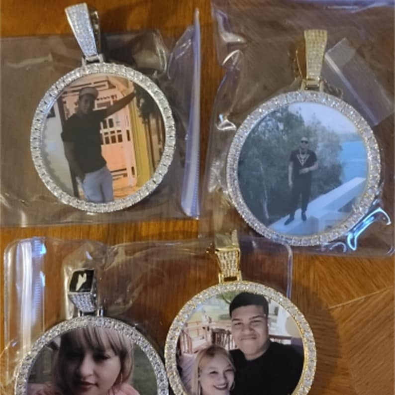 May include: Three gold-tone pendants with round photo inserts. Each pendant has a diamond-like design around the photo insert. The photos show different people.