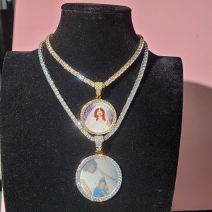 May include: Two gold tone oval photo pendants with clear cubic zirconia stones on a silver tone chain. The top pendant features a woman in a white dress and the bottom pendant features a woman and a child.