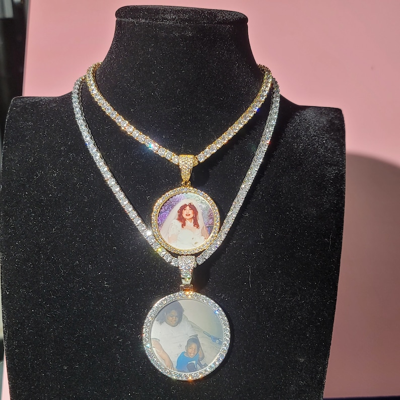 May include: Two gold tone oval photo pendants with clear cubic zirconia stones on a silver tone chain. The top pendant features a woman in a white dress and the bottom pendant features a woman and a child.