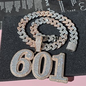 May include: A gold and silver chain necklace with a large pendant featuring the number 601 in sparkling rhinestones.