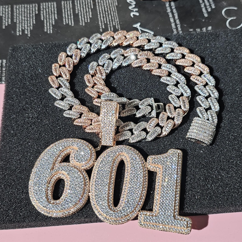 May include: A gold and silver chain necklace with a large pendant featuring the number 601 in sparkling rhinestones.