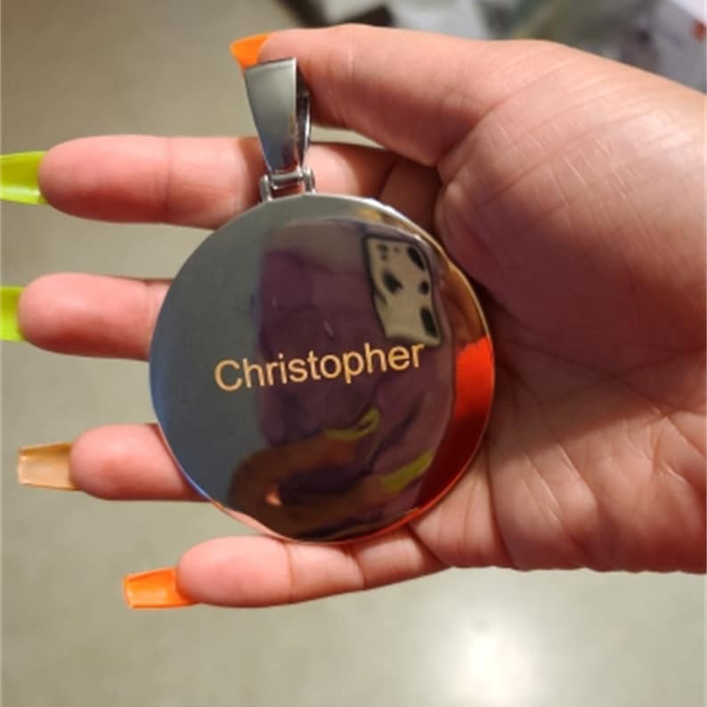 May include: A silver round pendant with a polished finish and the name "Christopher" engraved in gold lettering.