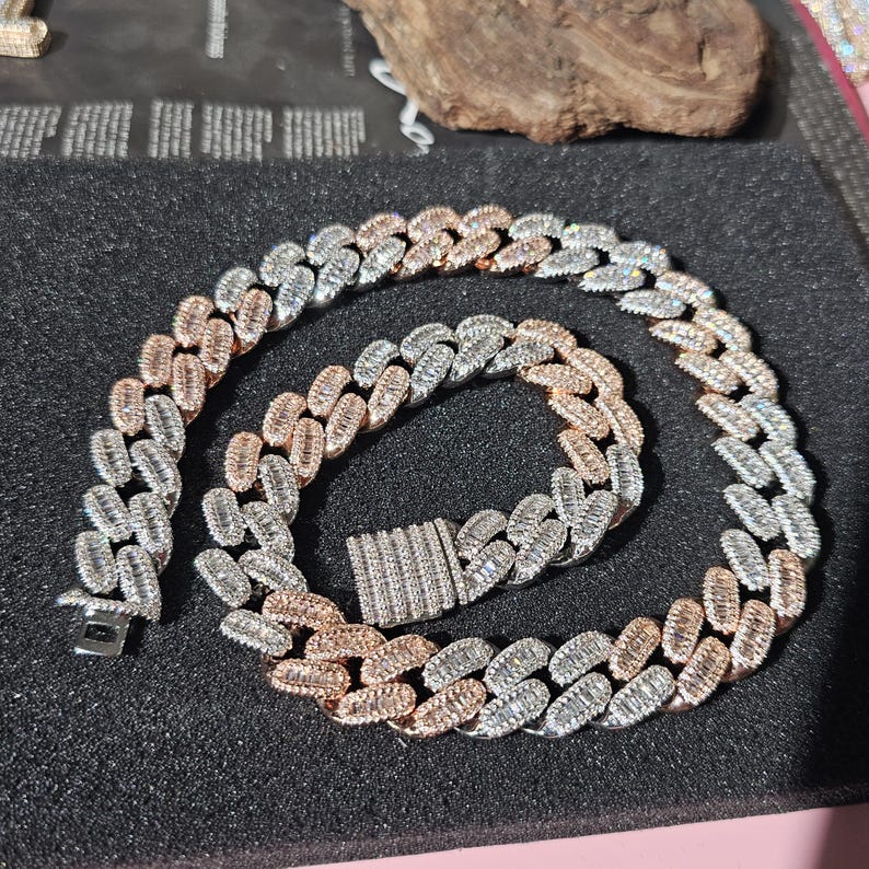 May include: A silver and rose gold chain necklace with baguette-cut cubic zirconia stones. The chain is a Cuban link style.