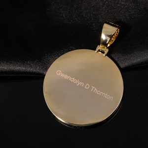 May include: A gold pendant with a round, smooth surface. The pendant is engraved with the name "Gwendolyn D Thornton".