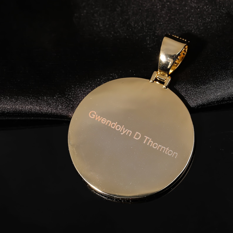 May include: A gold pendant with a round, smooth surface. The pendant is engraved with the name "Gwendolyn D Thornton".
