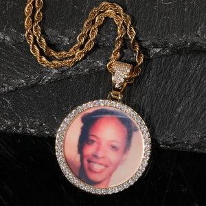 May include: A gold chain necklace with a round pendant featuring a photo of a woman. The pendant is surrounded by small clear stones.