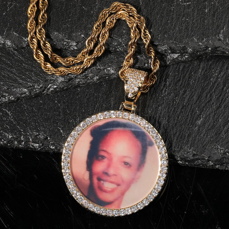 May include: A gold chain necklace with a round pendant featuring a photo of a woman. The pendant is surrounded by small clear stones.