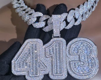 May include: A diamond-encrusted chain necklace with a large pendant featuring the number "413". The necklace has a thick, linked chain design. The pendant and chain sparkle with numerous small, clear gemstones, creating a luxurious appearance.