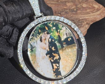 May include: A silver pendant with a circular design, encrusted with small, clear gemstones. The pendant features a photograph of a couple kissing. The bail is also covered in gemstones. A ruler is visible in the foreground.