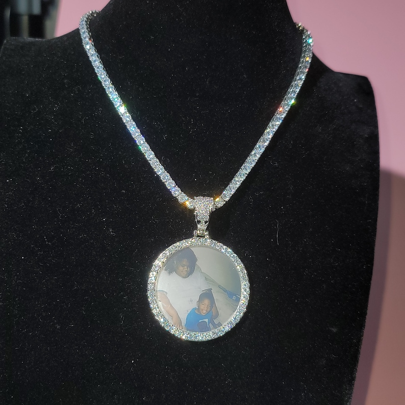 May include: A silver chain necklace with a round pendant featuring a photo of a woman and a child. The pendant is surrounded by small, clear stones.
