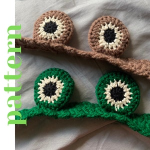 May include: Two crocheted eye patches, one brown and one green, with white and black details. The eye patches are attached to a crocheted headband.