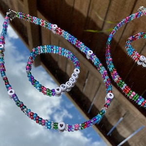 May include: A colorful beaded necklace and bracelet set with the word "SOUR" spelled out on the bracelet. The beads are in shades of blue, green, red, and pink.