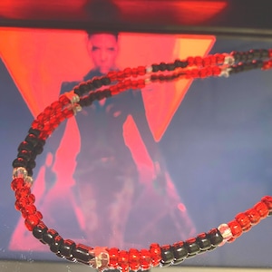 Puede incluir: Un collar de cuentas rojas y negras con detalles plateados. El collar está hecho de cuentas pequeñas y redondas y está en capas en una doble hebra.
