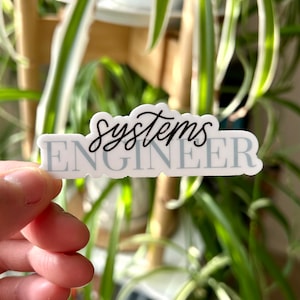 May include: A white sticker with a blue background and the text "systems engineer" in black cursive writing.