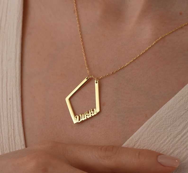 May include: Gold necklace with a geometric pendant featuring the name "Vikki" in a cursive font.