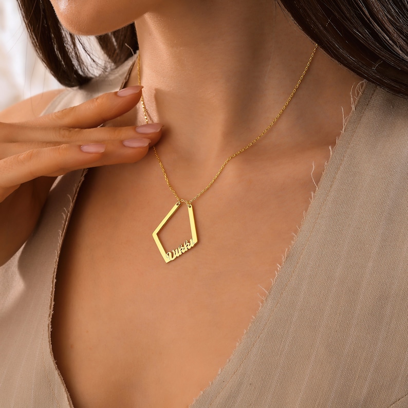 May include: A gold necklace with a diamond-shaped pendant that says "Dushka" in cursive.