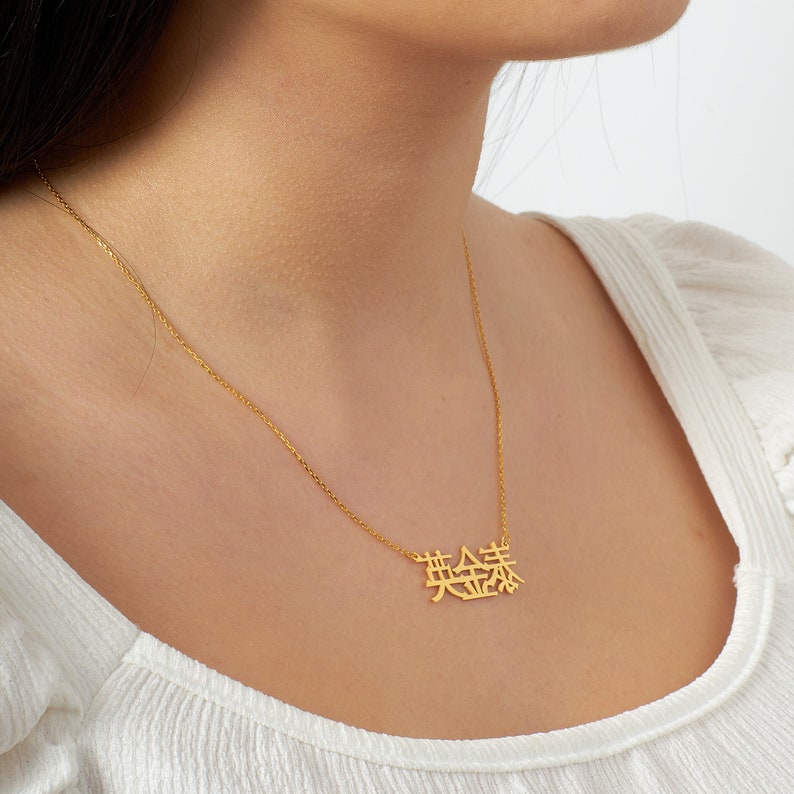 Peut inclure: Collier en or avec une cha&icirc;ne d&eacute;licate et un pendentif repr&eacute;sentant les caract&egrave;res chinois pour "chanceux" dans un style moderne et minimaliste.