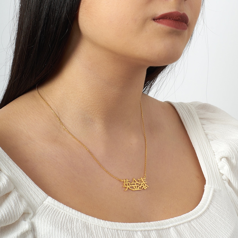 Peut inclure: Un collier en cha&icirc;ne dor&eacute;e avec un pendentif repr&eacute;sentant les caract&egrave;res chinois pour "amour" dans une police de caract&egrave;res stylis&eacute;e.