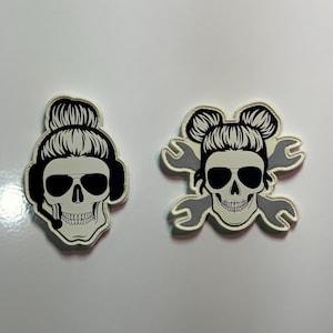 May include: Two black and white skull patches with a white background. One skull is wearing sunglasses and a headset. The other skull is wearing sunglasses and has two wrenches crossed behind it.