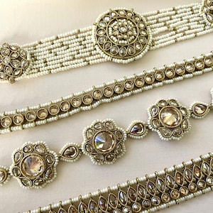 May include: Four gold and white beaded necklaces with decorative crystal accents. The necklaces feature different styles of crystal embellishments, including round, teardrop, and flower shapes.