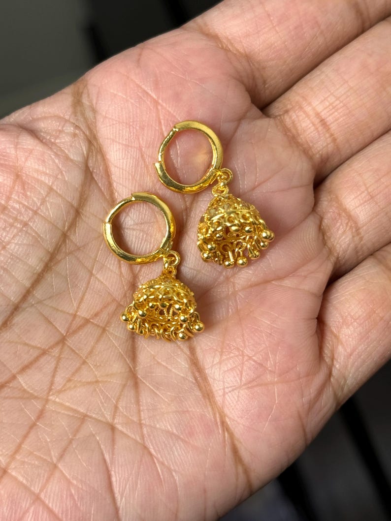 May include: A pair of gold hoop earrings with small, dangling bells. The bells are made of tiny gold beads.
