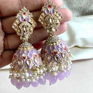 May include: A pair of purple and gold dangle earrings with white pearl and lavender beads. The earrings feature a detailed design with intricate floral patterns and clear rhinestones.